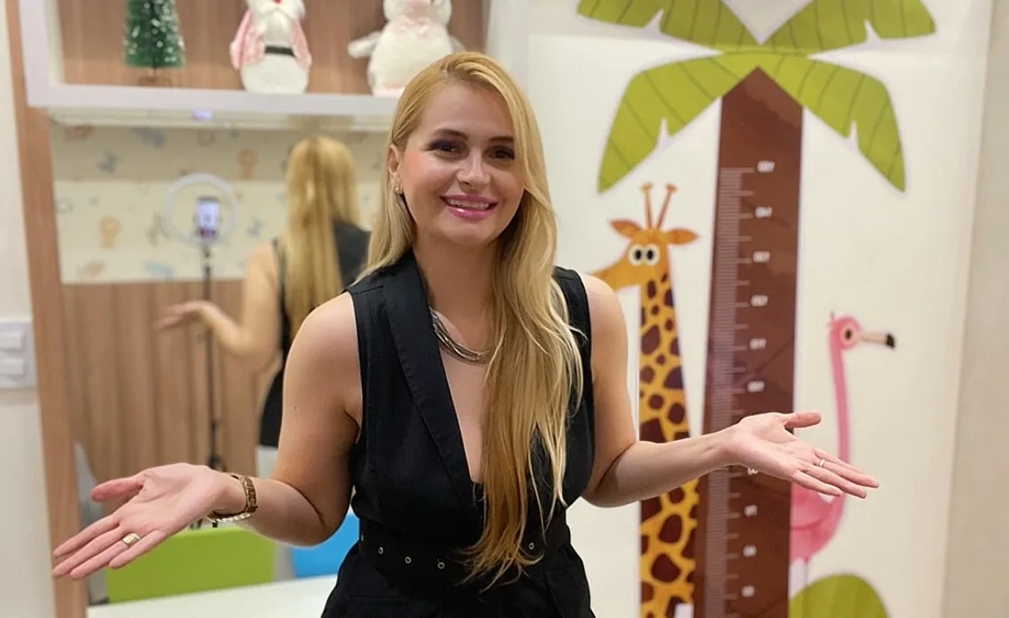 Priscila sorrindo de braços abertos no consultório infantil
